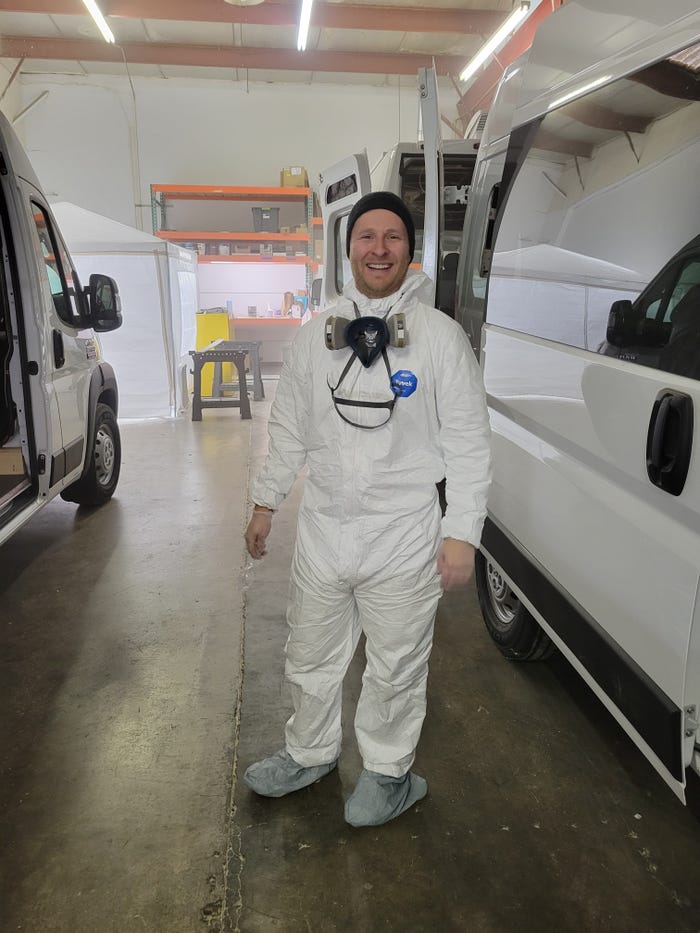 Singer in a white hazmat suit with goggles during van construction.