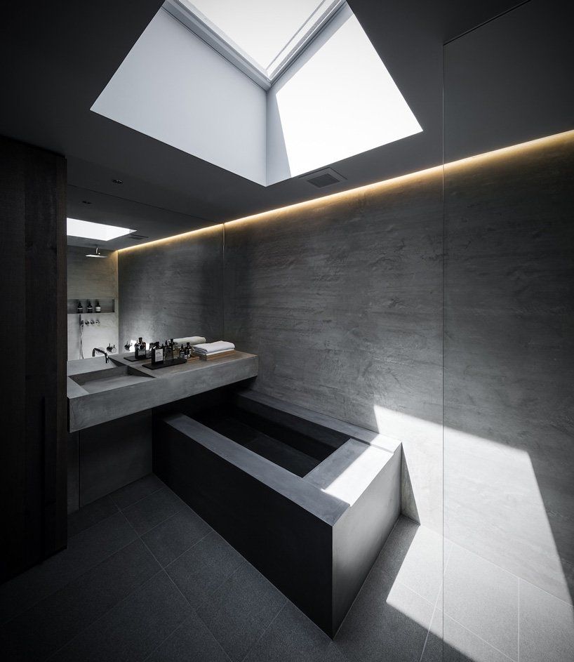 All-concrete bathroom with an angular concrete bath tub and skylight overhead. 